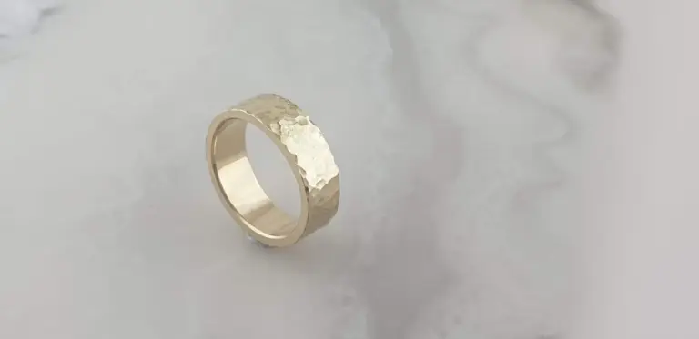 Close-up of a gold hammered wedding band on a soft, light grey surface.