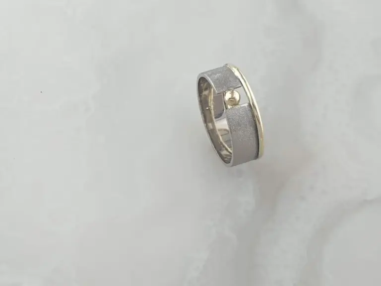 Close-up of a metallic ring with a textured matte surface and a shiny, polished edge, set against a plain, light background.