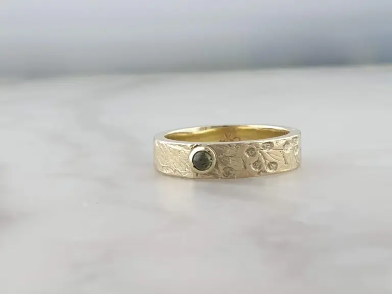 A gold ring with a textured surface and a black gemstone embedded in it, placed on a white surface.