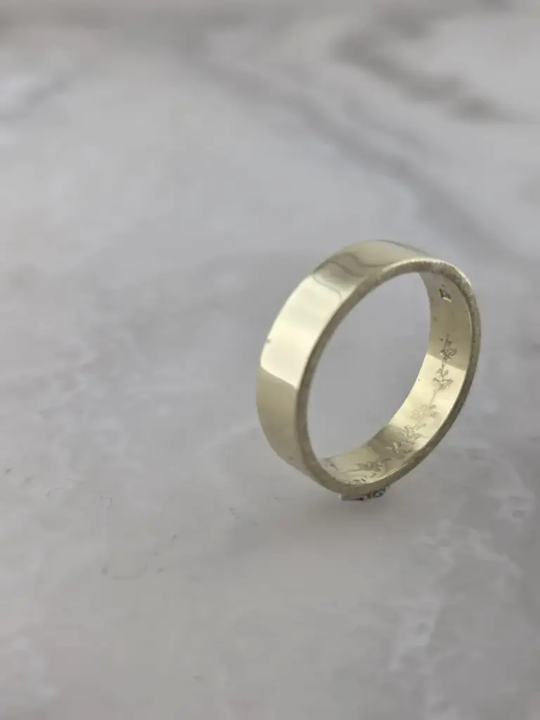 Silver ring with engraved floral designs on a gray surface.