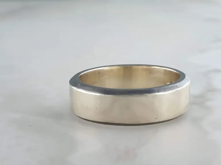 Close-up of a metallic ring with a gold-colored interior, resting on a plain surface.