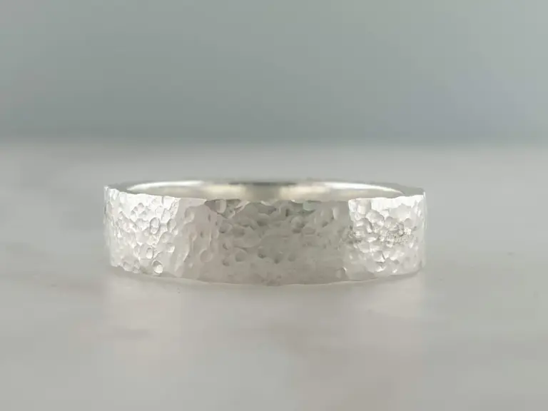 Close-up of a textured silver ring with a hammered finish, shown against a plain background.