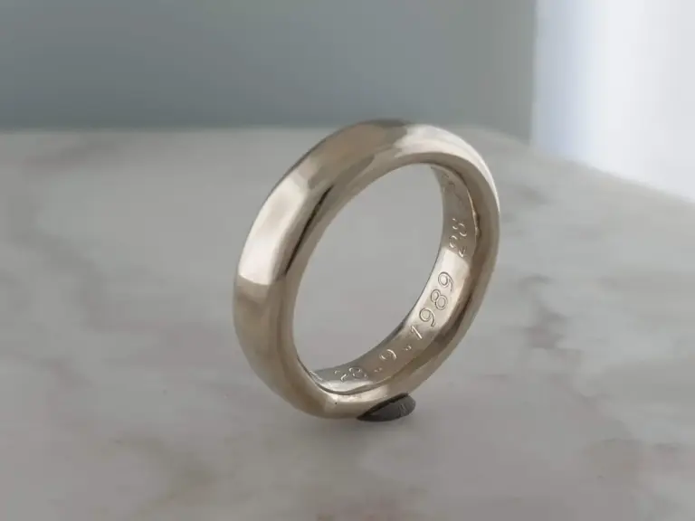 Close-up of a shiny silver ring with engraved numbers and letters, resting on a small piece of material on a white surface.
