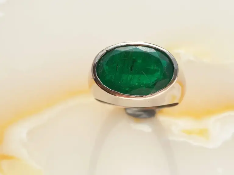 A silver ring with a large, oval-shaped green gemstone set in the center, resting on a light-colored surface.