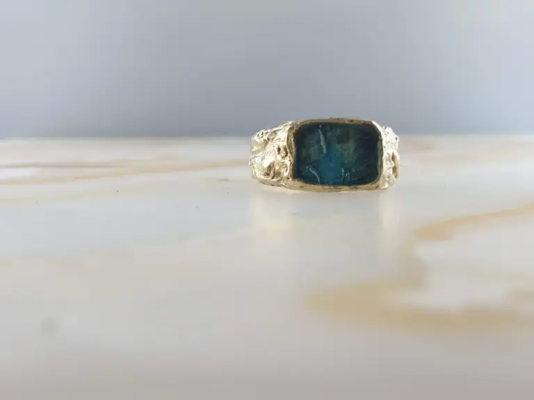 A silver ring with a rectangular dark blue gemstone set in a textured band, placed on a light-colored surface with a plain background.