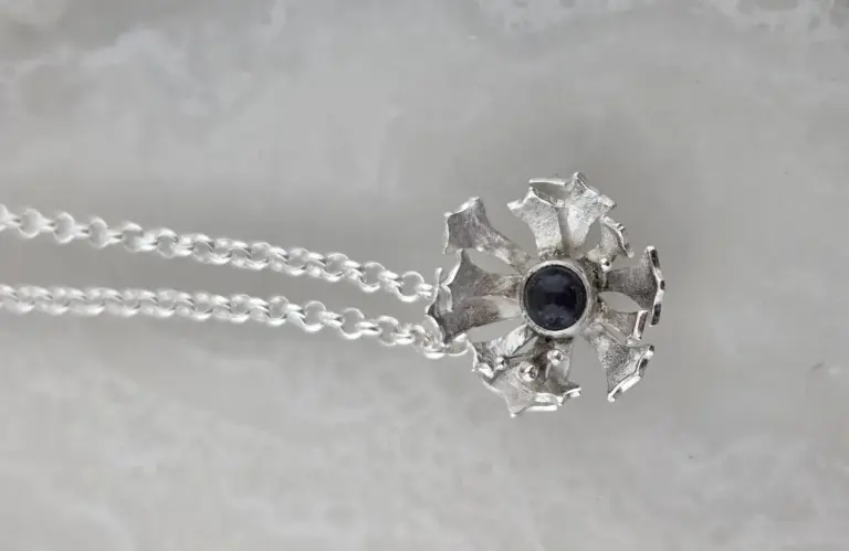 Silver necklace with a pendant shaped like a six-pointed star with a black gemstone at the center, on a light gray background.
