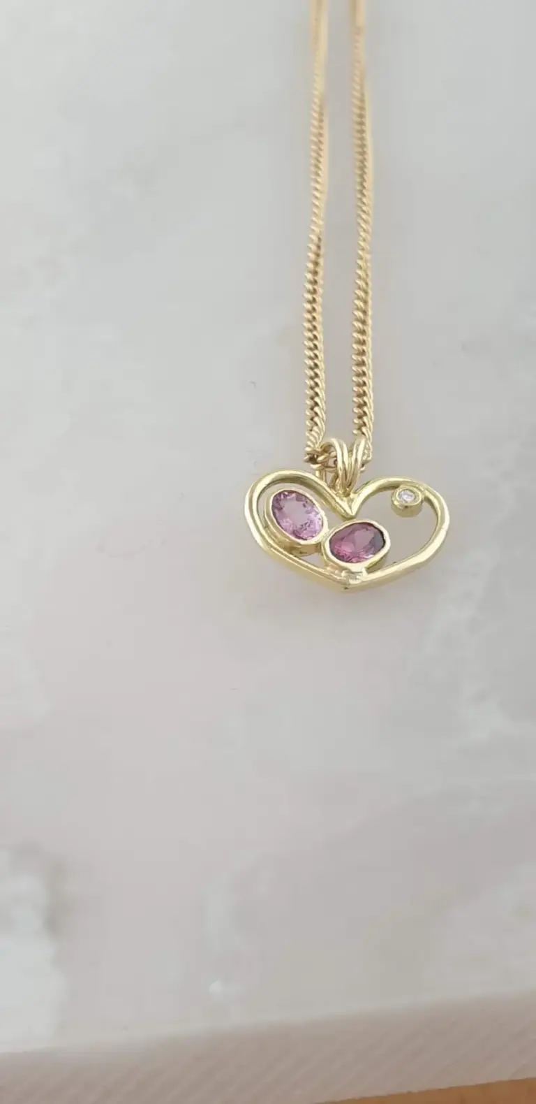 Gold heart-shaped necklace with pink gemstones and a small clear gemstone pendant.