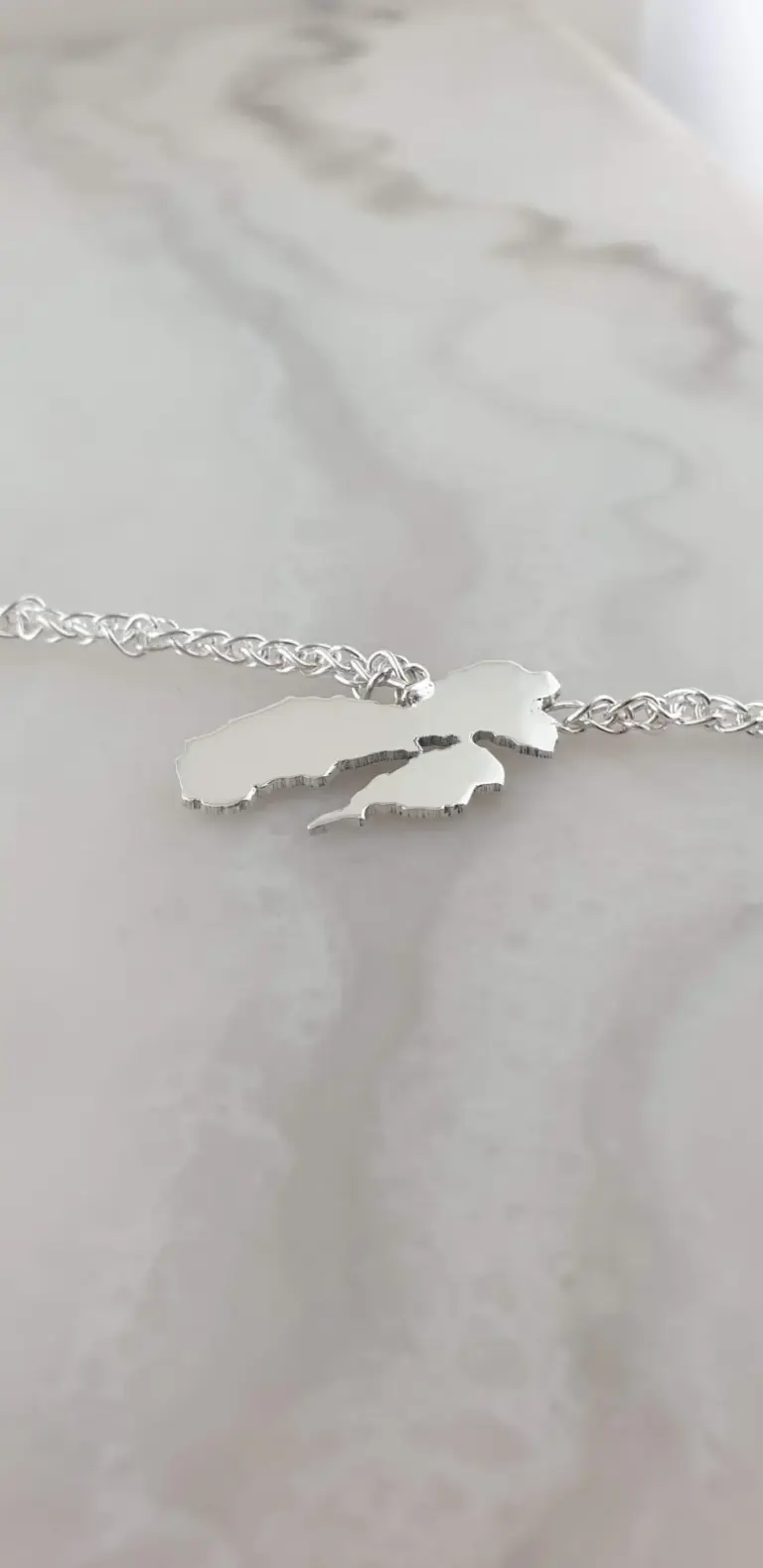 Silver necklace with a pendant in the shape of Michigan's map on a marble surface.