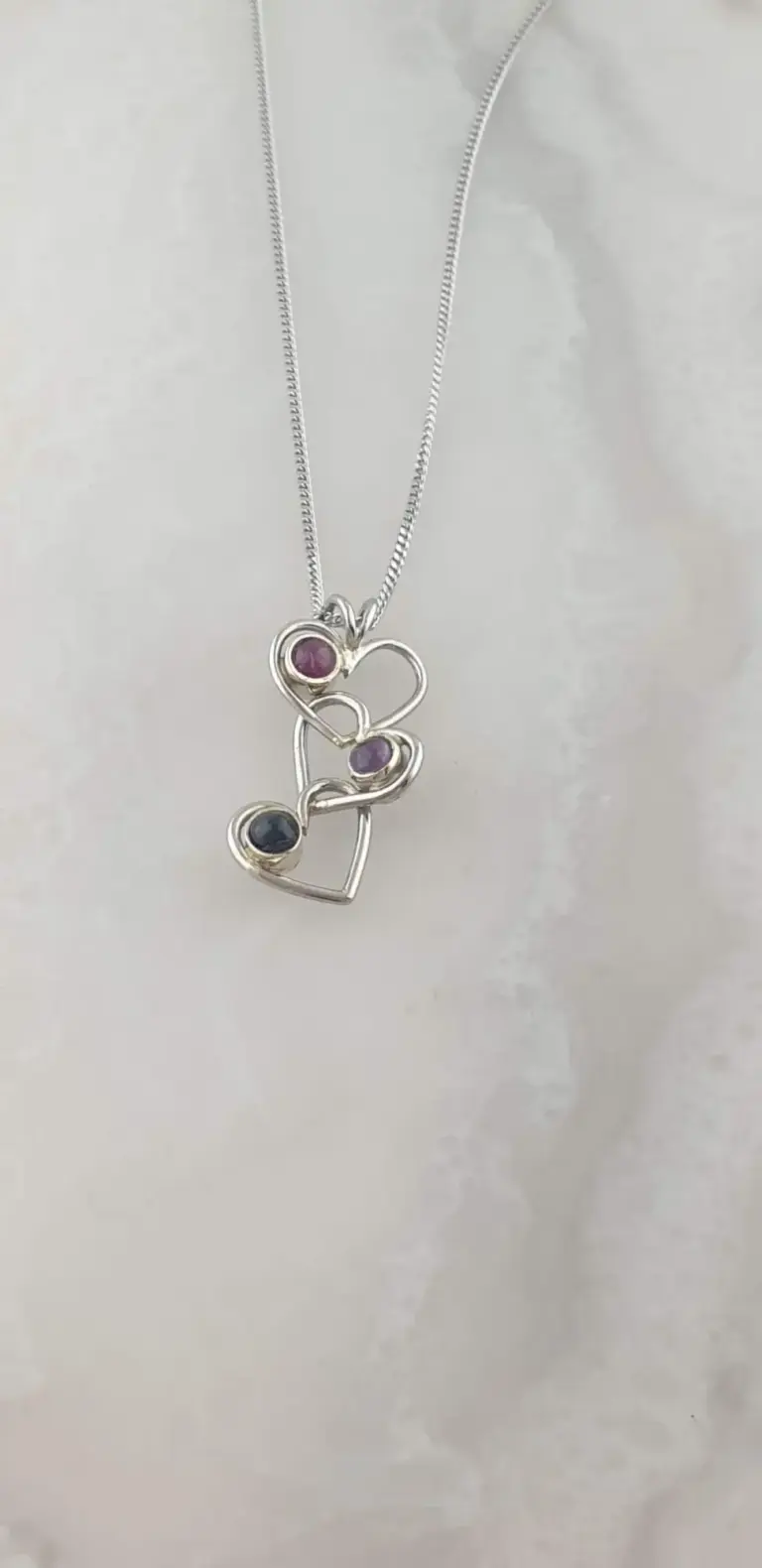 Silver necklace with a pendant consisting of multiple interconnected hearts and circular stones in pink, purple, and black.