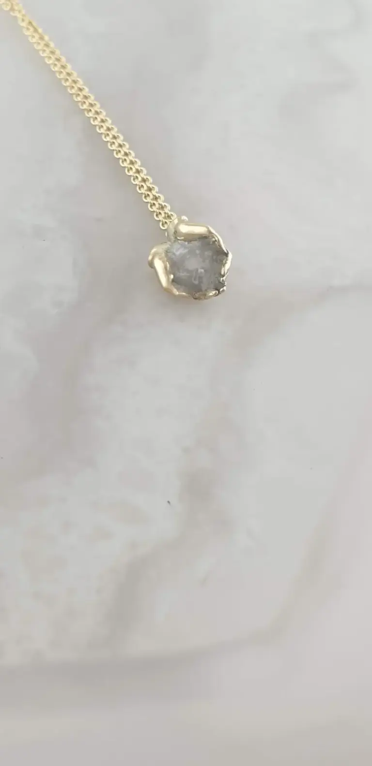 Silver necklace with a raw, uncut gemstone pendant resting on a white surface.