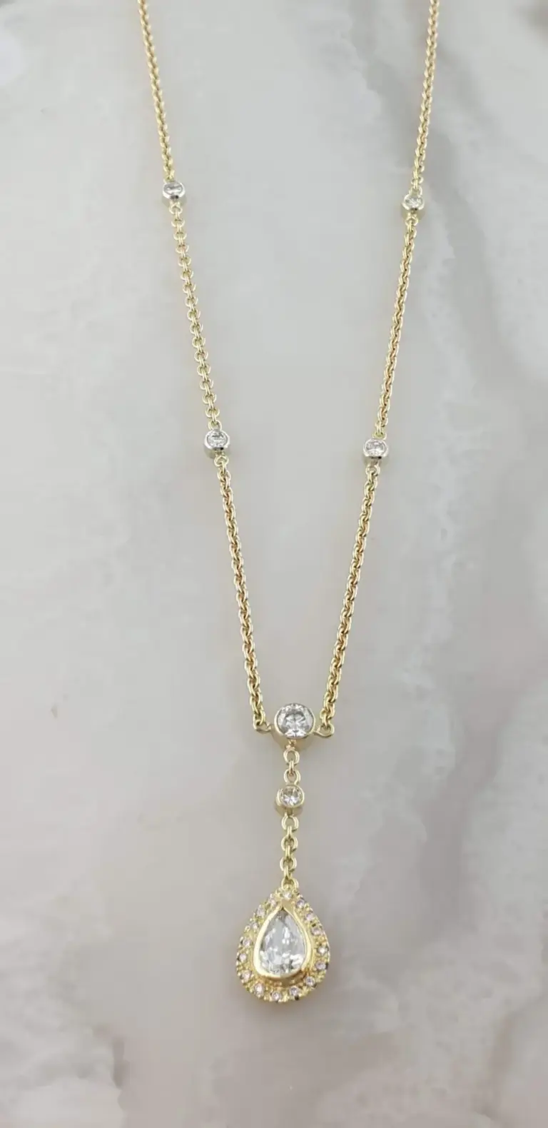 Gold and diamond pendant necklace with a teardrop-shaped diamond surrounded by smaller diamonds.