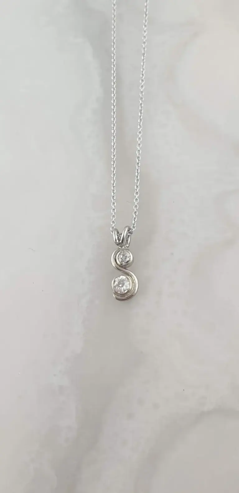 Silver necklace with a pendant featuring a stylized letter 'S' decorated with two small diamonds.