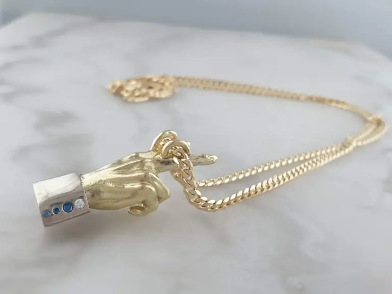 Close-up of gold jewelry on white marble surface, including a chain, a ring, and a piece with embedded gemstones.