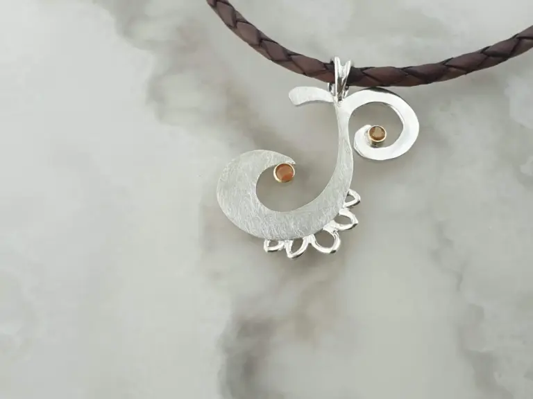 A silver pendant necklace shaped like a seahorse with two orange stones, hanging from a braided brown leather cord.