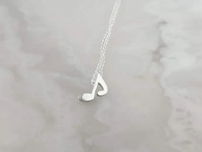 A silver necklace with a pendant shaped like a musical note, hanging against a plain background.