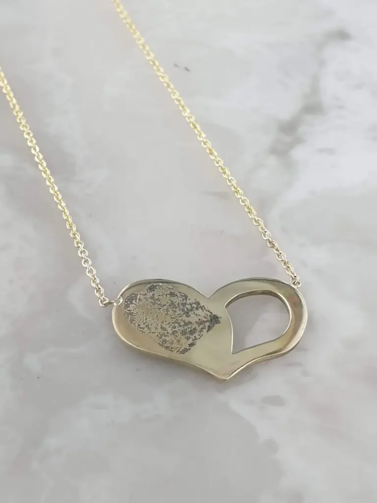 A gold necklace with a heart-shaped pendant on a white marble surface.
