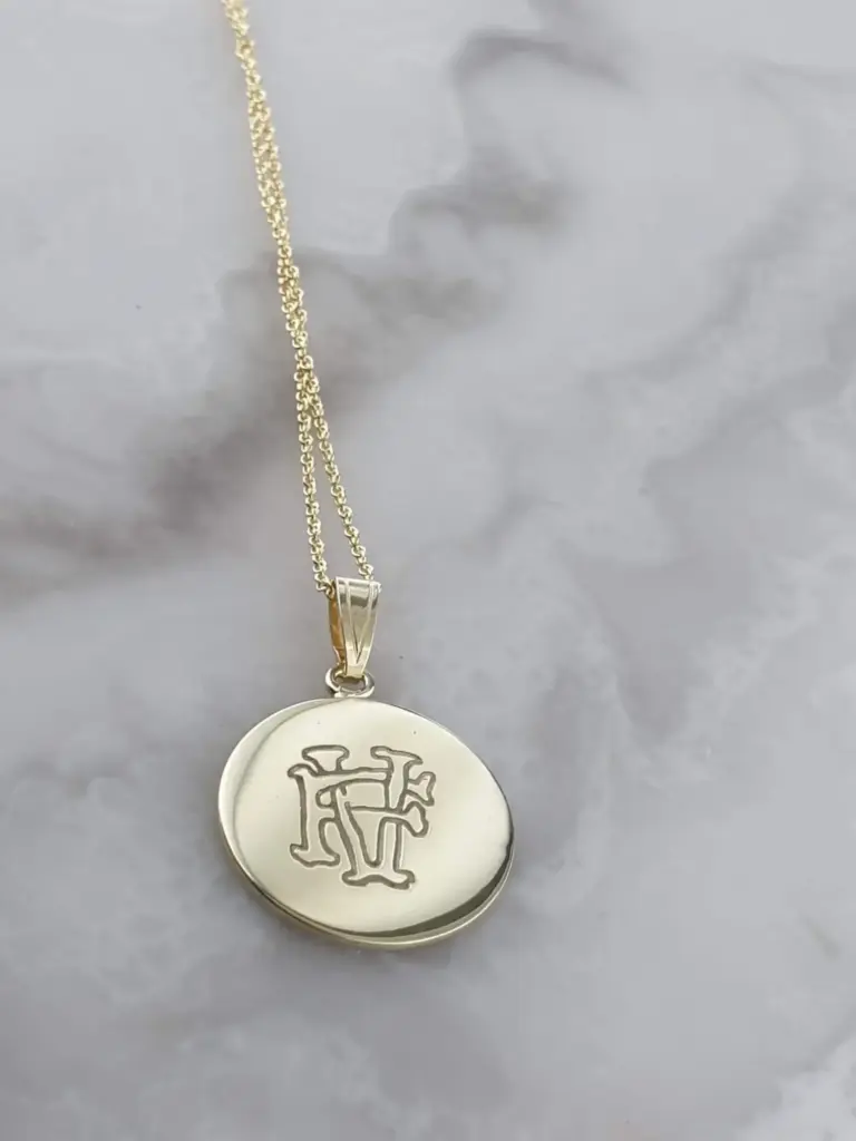 Silver necklace with a round pendant engraved with Chinese characters, lying on crumpled white paper.