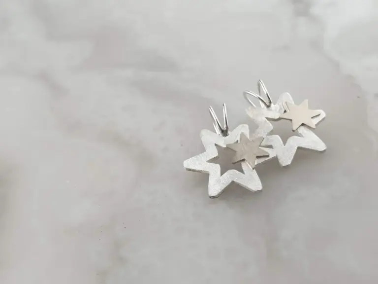A close-up of silver and white Christmas snowflake-shaped earrings on a white background.