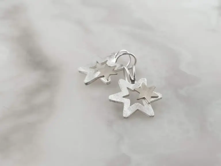 Close-up of silver star-shaped and heart-shaped earrings on a reflective surface.