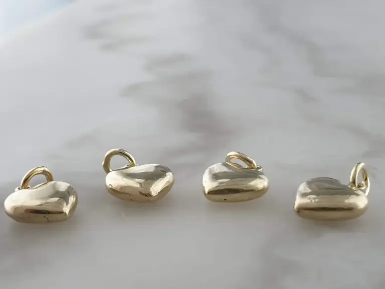 A collection of silver heart-shaped charms with gold loops, placed on a white surface.