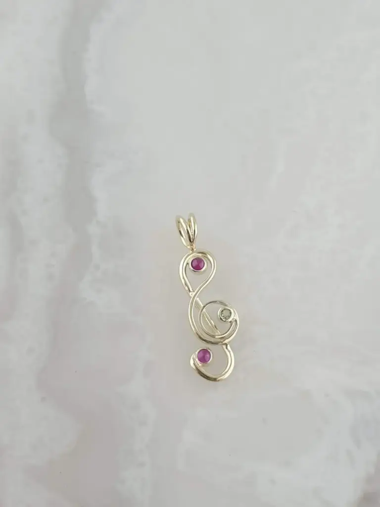 A silver necklace pendant with a treble clef shape, featuring pink gemstones at three points.