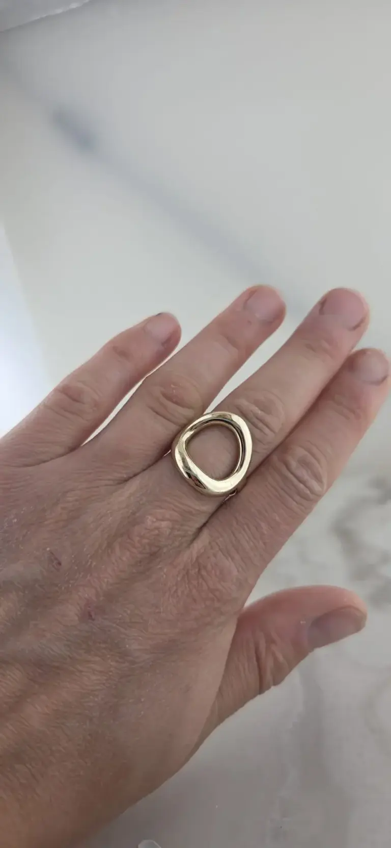 Close-up of a person's hand with a large gold ring on the middle finger.