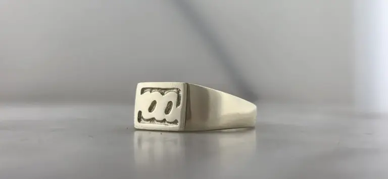 Metal ring with engraved smiley face design on the top, positioned on a smooth surface with a plain background.