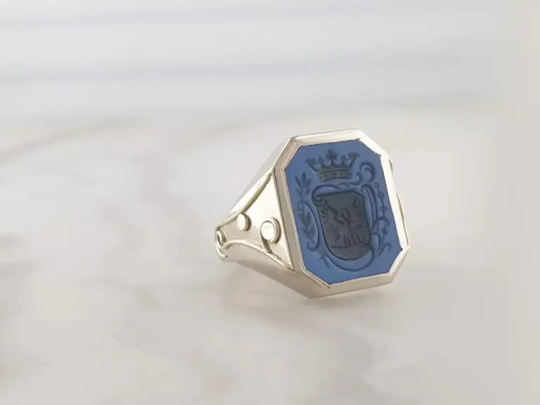 Close-up of a silver ring with a blue face featuring a lion's head and a crown above it.