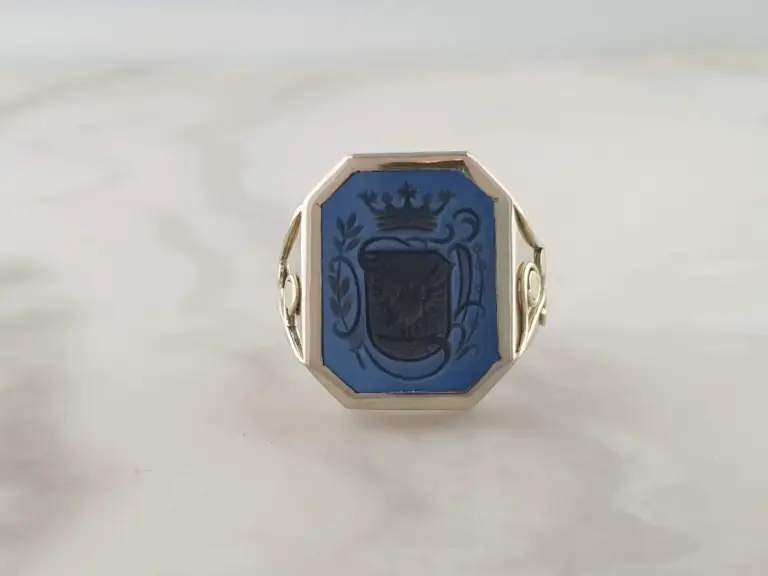 Close-up of a ring with a blue gemstone featuring a crest with a crown and decorative elements.