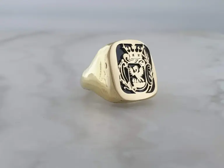 Close-up of a signet ring with a black design featuring a crowned figure and intricate detailing, set against a plain, light gray background.