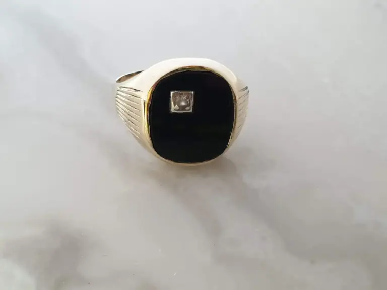 A silver signet ring with a black oval face and a small square silver element in the center, against a plain white background.