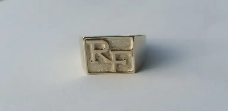 Silver square ring with raised block letters spelling 'RIE' on its surface.