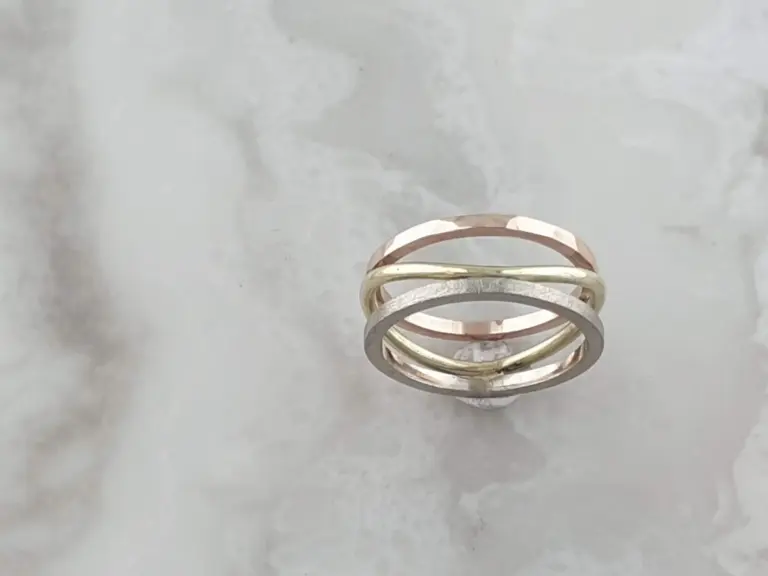 Stacked rings in gold, rose gold, and silver on a gray surface.