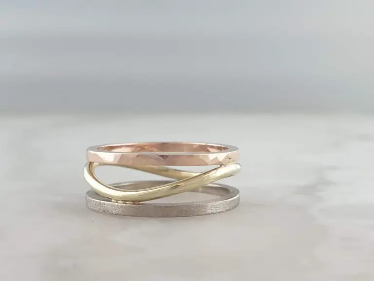 Several stacked thin rings in silver, rose gold, and gold colors on a plain, light-colored background.