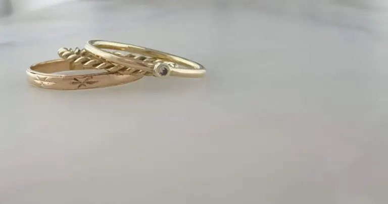 Three gold rings, one with a small gemstone, arranged on a plain white surface.