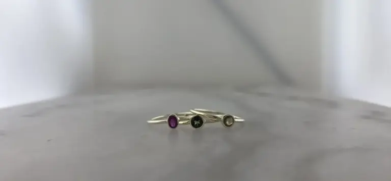 Three stacked rings with colored stones, one purple, one black, and one clear, on a plain gray surface.
