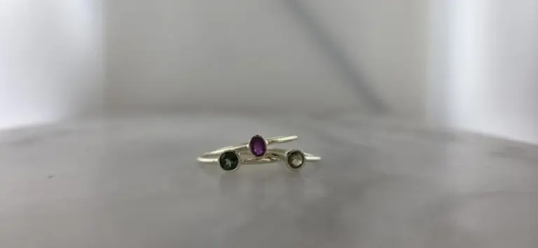 Three silver rings with colored gemstones on a plain gray surface