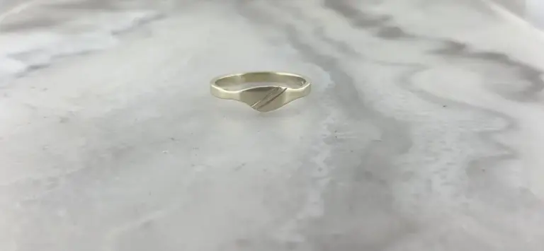 A silver ring with a diagonal stripe pattern, lying on a smooth, light-colored surface.