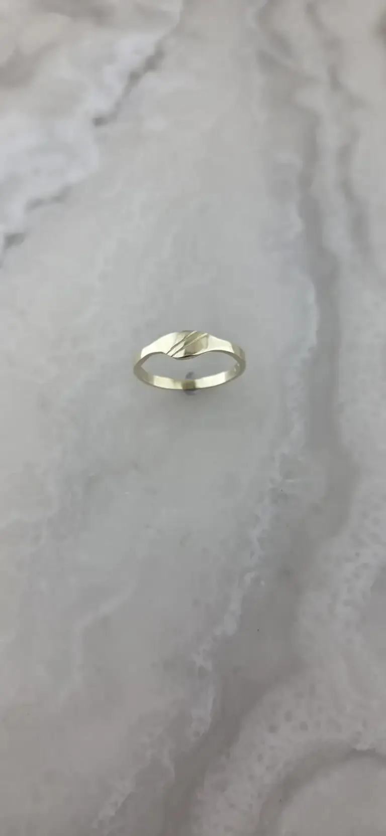 A silver ring with a wave pattern on a white marble surface.