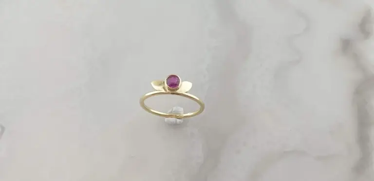 Gold ring with an oval purple gemstone, displayed on a white textured background.