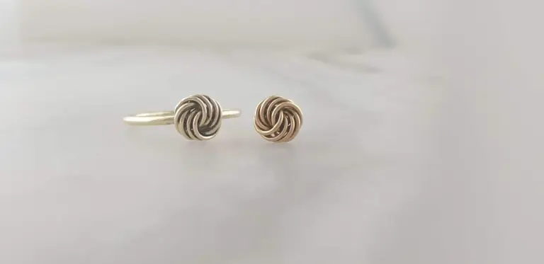 Silver ring and gold earrings with intricate knot design on a light background.
