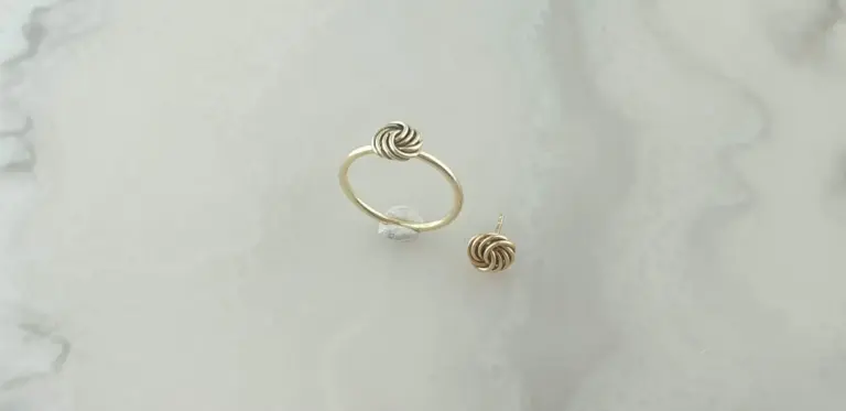 A gold ring and matching gold stud earrings with knotted designs on a white marble surface.