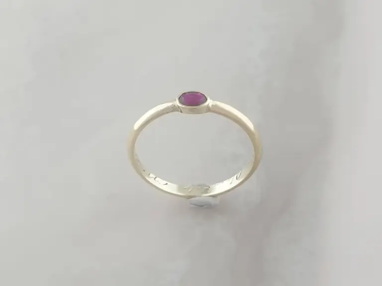 A silver ring with a purple gemstone on a plain white background.
