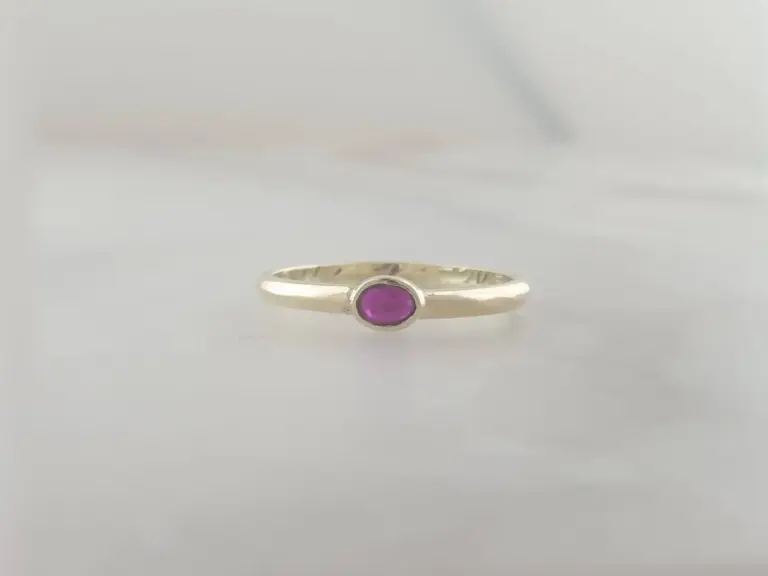 A silver ring with a purple gemstone set in the center, displayed against a plain background.