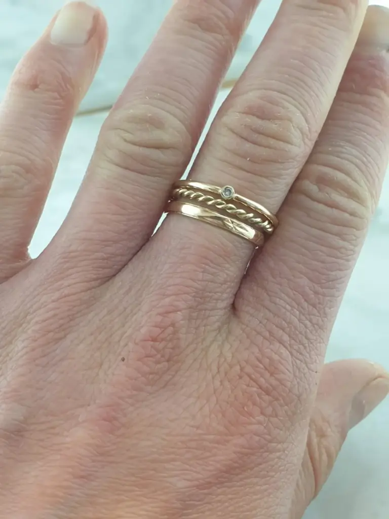 Close-up of a person's hand with three gold rings, one featuring a small gemstone, on the ring finger.