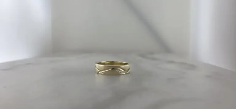 A gold ring with a curved design, placed on a white surface against a plain white background.