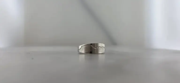 A silver ring with a textured outer surface and smooth inner surface, placed on a white surface against a plain white background.
