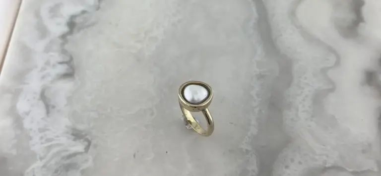 A gold ring with a white gemstone is placed on a marble surface.