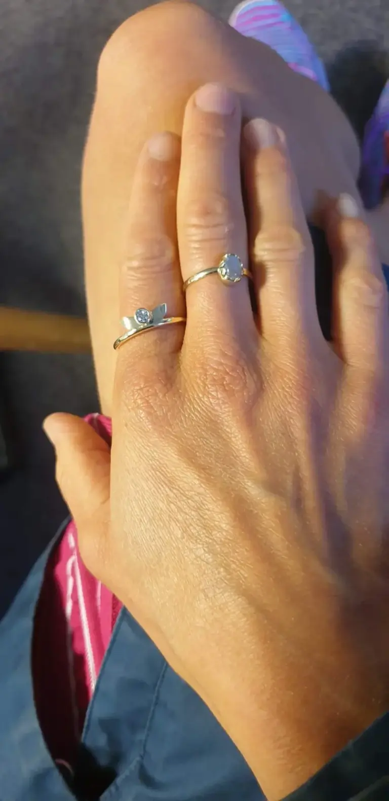 Close-up of a person's hand showing two rings with large stones on the middle and index fingers.