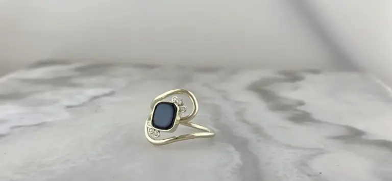 A silver ring featuring an oval-shaped dark stone surrounded by small clear gemstones, set on a marble surface.